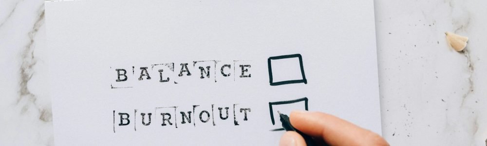 Close-up of a hand hovering over a checklist with options for balance or burnout, symbolizing stress and choice.